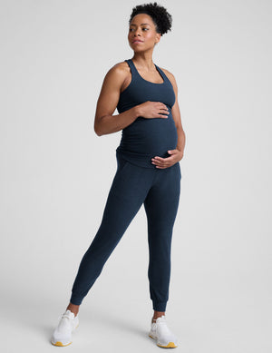 pregnant woman wearing a navy blue racerback maternity tank and maternity joggers with pockets on a plain background. 