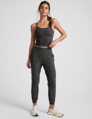 woman wearing a dark gray tank top and joggers on a plain background. 