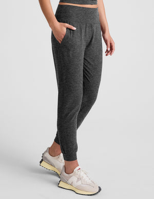 woman wearing a dark gray joggers on a plain background. 