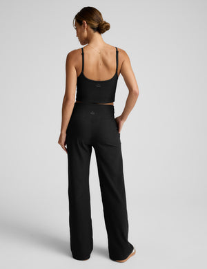 Woman wearing a black tank top and pants on a light gray background. 