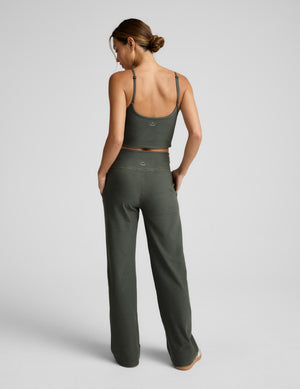 Back facing image of a woman wearing a green mid length tank top and wide leg pants against a plain background. 