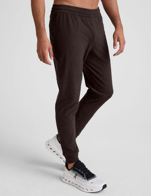 male model wearing brown men's joggers with zipper pockets on a plain background. 