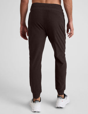 male model wearing brown men's joggers with zipper pockets on a plain background. 