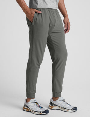 man wearing a gray shirt and gray pants on a plain background. 