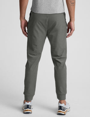 man wearing a gray shirt and gray pants on a plain background. 