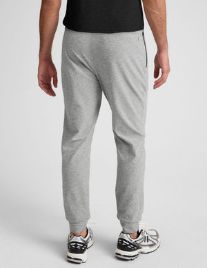 man wearing a black t-shirt and gray sweatpants on a plain background. 