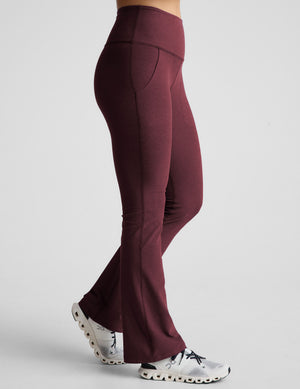 model wearing maroon bootcut pants with pockets on a light gray background. 
