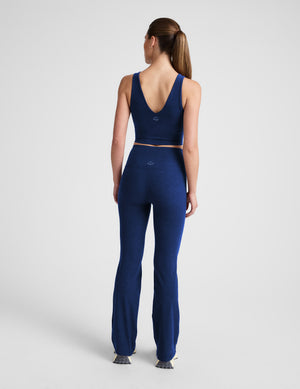 Woman wearing a blue v-neck cropped tank and bootcut pants with pockets on a plain background. 