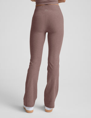 Woman wearing brown bootcut pants with pockets against a light gray background. 