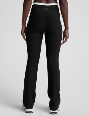 Woman wearing black bootcut pants with a white lining at waistband on a plain background. 