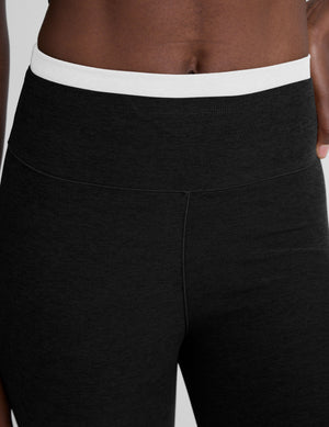 Woman wearing black bootcut pants with a white lining at waistband on a plain background. 