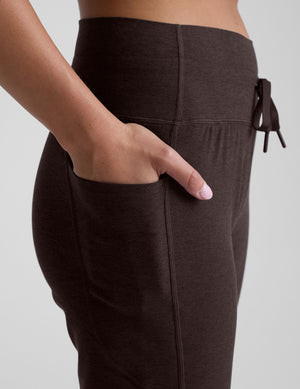 brown pants with a hand in one of the pockets on a light gray background. 