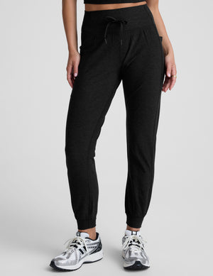 model wearing black high-waisted midi length joggers with a drawcord at waistband and pockets against a plain background. 