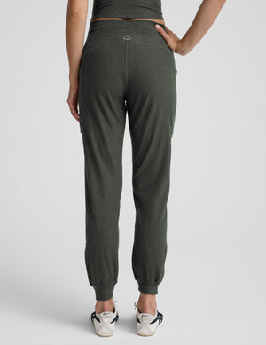 Woman wearing green midi length joggers with a drawstring at waistband on a plain background. 