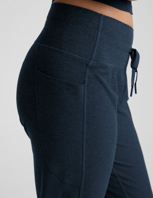 model wearing navy blue high-waisted midi length joggers with a drawcord at waistband and pockets athletic outfit on a plain background. 