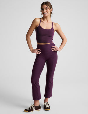 Woman wearing a purple cropped tank and purple kick flare pants against a plain background. 