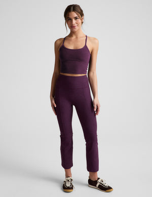 Woman wearing a purple cropped tank and purple kick flare pants against a plain background. 
