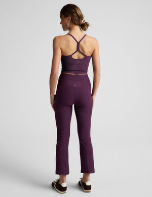 Woman wearing a purple cropped tank and purple kick flare pants against a plain background. 