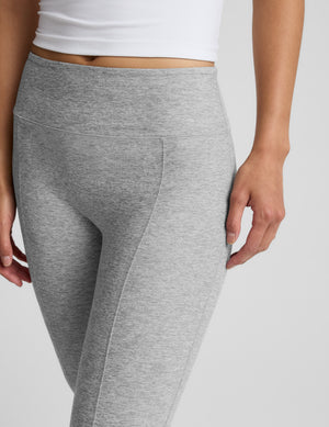 Woman wearing a white waist length tank and gray kickflare pants against a plain background. 