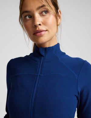 Woman wearing a blue zip-up athletic jacket and leggings on a light background. 