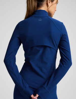 Woman wearing a blue zip-up athletic jacket and leggings on a light background. 