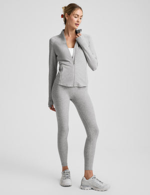 Woman wearing a gray zip-up jacket and legging on a light gray background. 