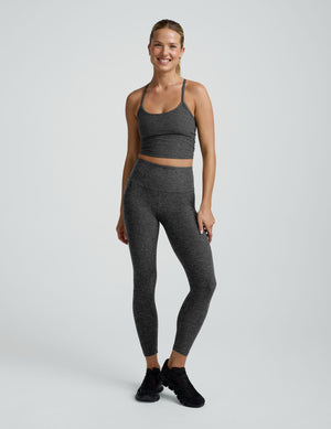woman wearing a gray cropped tank and long length leggings on a plain background. 