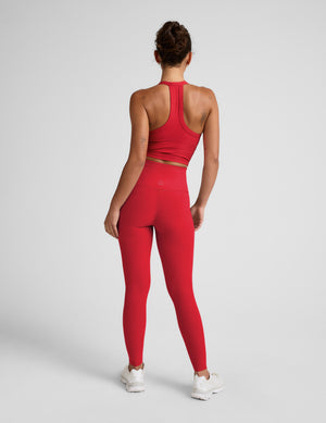 Woman wearing a red cropped tank and high-waisted full length leggings on a plain background. 