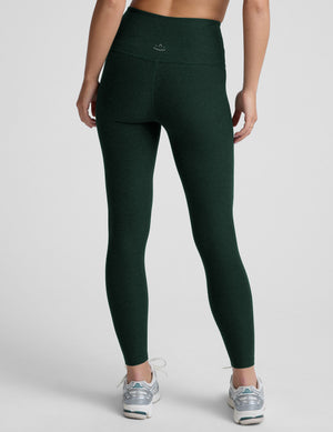 model wearing green high-waisted full length leggings on a plain background. 