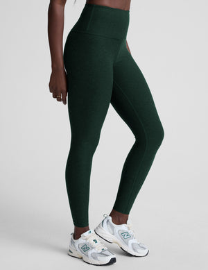 model wearing green high-waisted full length leggings on a plain background. 