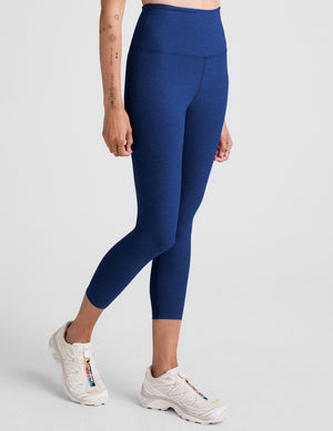 Woman wearing blue high-waisted capri leggings on a light gray background. 