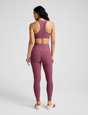 Woman wearing a matching purple sports bra and leggings set on a light gray background. 