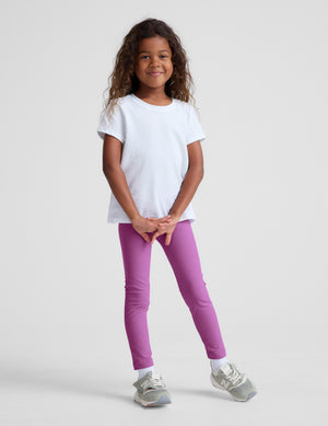Child wearing a white t-shirt and purple pants on a plain background. 