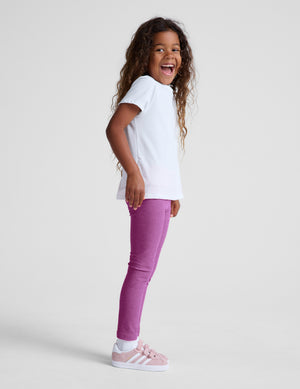 Child wearing a white t-shirt and purple pants on a plain background. 