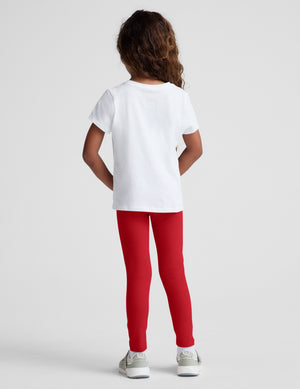 toddler wearing a white t-shirt and red leggings against a plain background. 