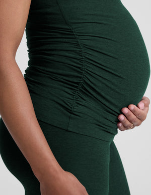 model wearing a green maternity racerback tank and green maternity midi length leggings on a plain background. 