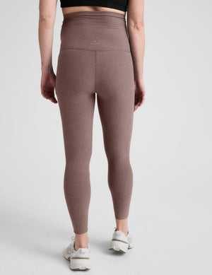 Pregnant woman wearing brown leggings on a white background. 