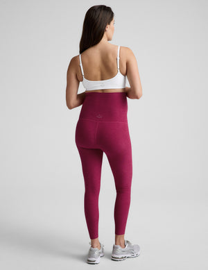 Pregnant woman wearing pink leggings and a white top on a light gray background. 