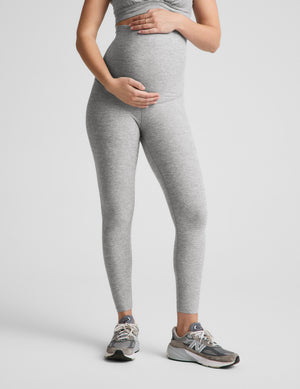 Pregnant woman wearing a gray bra and leggings on a plain background. 