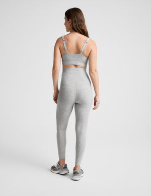 Pregnant woman wearing a gray bra and leggings on a plain background. 