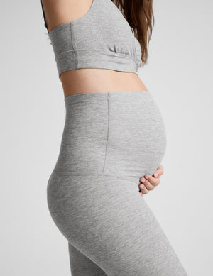 Pregnant woman wearing a gray bra and leggings on a plain background. 