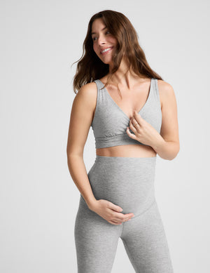 Pregnant woman wearing a gray bra and leggings on a plain background. 