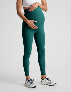 Woman wearing green maternity leggings on a light gray background. 