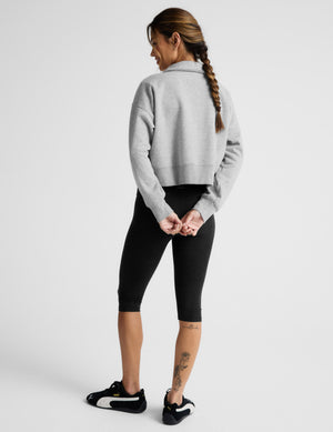 Woman wearing a black bra and black pedal pusher leggings against a plain background. 