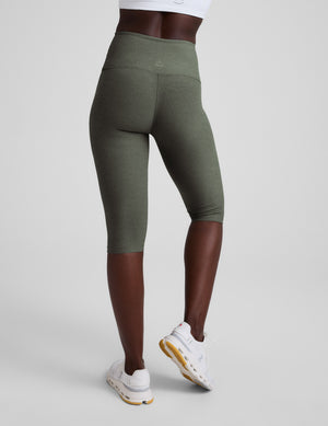 Woman wearing green pedal pusher leggings on a light gray background. 