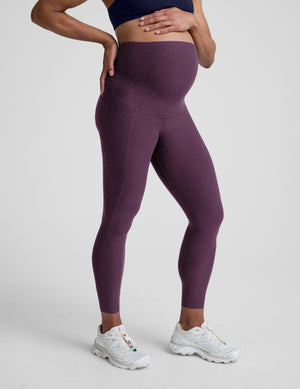 Woman wearing a purple maternity pocket leggings against a plain background. 