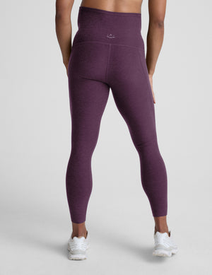 Woman wearing a purple maternity pocket leggings against a plain background. 