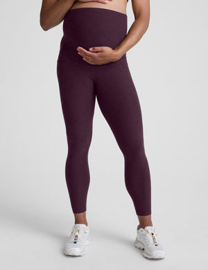 pregnant woman wearing maternity leggings with pockets against a plain background. 
