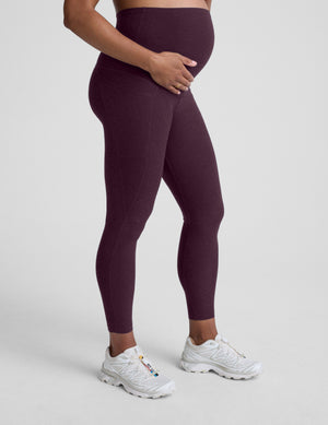 pregnant woman wearing maternity leggings with pockets against a plain background. 