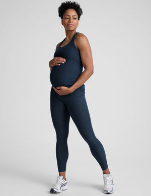 Pregnant woman wearing a navy blue tank top and leggings on a white background. 